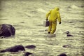 Technician in protective suit walking in water at rocky beach