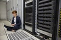 Technician sitting on floor beside server tower using laptop Royalty Free Stock Photo