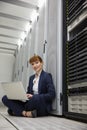 Technician sitting on floor beside server tower using laptop Royalty Free Stock Photo