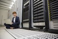 Technician sitting on floor beside server tower using laptop Royalty Free Stock Photo