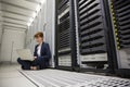 Technician sitting on floor beside server tower using laptop Royalty Free Stock Photo