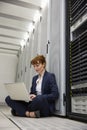 Technician sitting on floor beside server tower using laptop Royalty Free Stock Photo