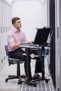 Technician sitting on swivel chair using laptop to diagnose servers