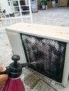 A technician spraying a chemical substance on air conditioner compressor using water dispenser pump.