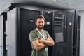IT technician standing in a data center server room with racks and network equipment, confident engineer Royalty Free Stock Photo