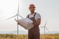 Technician standing of windmill farm with blueprints