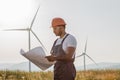 Technician standing of windmill farm with blueprints