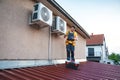 Technician using smartphone while installing air conditioners on building rooftop Royalty Free Stock Photo