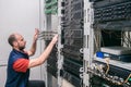 Technician was crouched down near computer racks. Engineer installs new switches in the server room. A man sets up server hardware