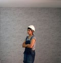 Technician woman ware white helmet with grey T-shirt and denim jeans apron dress standing forty five angle and hugging chest.