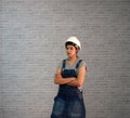 Technician woman ware white helmet with grey T-shirt and denim jeans apron dress standing forty five degree angle and hugging ches