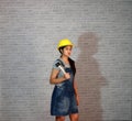 Technician woman ware yellow helmet with grey T-shirt and denim jeans apron dress standing and rubber hammer in hand.