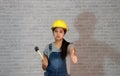 Technician woman ware yellow helmet with grey T-shirt and denim jeans apron dress standing with rubber hammer in hand. Royalty Free Stock Photo