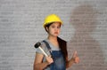 Technician woman ware yellow helmet with grey T-shirt and denim jeans apron dress standing with rubber hammer in hand and thumbs. Royalty Free Stock Photo