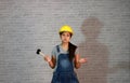 Technician woman ware yellow helmet with grey T-shirt and denim jeans apron dress standing and rubber hammer in right hand, palms