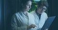 Technicians in lab coats tapping laptop while colleague checking server racks in aisle, green LEDs Royalty Free Stock Photo