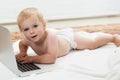 Technologically minded. Cute baby playing with a laptop while lying on the floor.