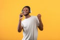 Technologies for fun. Overjoyed african american guy listening music in headphones and singing over yellow background Royalty Free Stock Photo