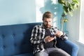 Technologies and leisure concept - Cheerful man sitting on the couch using his smartphone at home in the living room. Royalty Free Stock Photo