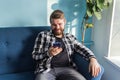 Technologies and leisure concept - Cheerful man sitting on the couch using his smartphone at home in the living room. Royalty Free Stock Photo