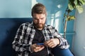 Technologies and leisure concept - Cheerful man sitting on the couch using his smartphone at home in the living room. Royalty Free Stock Photo