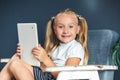 Technologies, people concept - young blondy girl sitting on a chair and watching the tablet or surfing the net, looking at camera