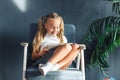 Technologies, people concept - young blondy girl sitting on a chair and watching the tablet or surfing the net and smiling