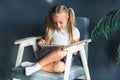 Technologies, people concept - young blondy girl sitting on a chair and watching the tablet or surfing the net and smiling