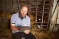 Technology can help in any industry. a male farmer using a tablet while sitting in a barn on his dairy farm. Royalty Free Stock Photo