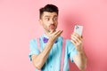 Technology concept. Funny man sending air kiss on video chat, blowing mwah at smartphone camera, standing on pink Royalty Free Stock Photo