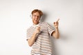 Technology concept. Happy redhead man listening music in headphones and dancing and pointing fingers right, standing Royalty Free Stock Photo