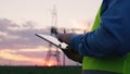 technology concept with high voltage power lines. electrical engineer helmet digital tablet sunset. power engineer power Royalty Free Stock Photo
