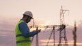 technology concept with high voltage power lines. electrical engineer helmet digital tablet sunset. power engineer power Royalty Free Stock Photo