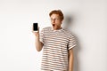 Technology and e-commerce concept. Surprised and shocked redhead guy checking out online promotion, showing blank