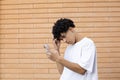 A puzzled male African-American student holding a phone and solving a task in mind during an online meeting