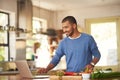 Technology has its place in the kitchen. Shot of a happy young man using a laptop while preparing a healthy meal at home Royalty Free Stock Photo