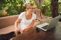 Happy senior woman with home cat use wireless headphones working online with laptop computer outdoor Royalty Free Stock Photo