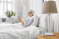 senior woman with smartphone and earphones in bed Royalty Free Stock Photo