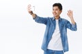 Technology, online lifestyle concept. Hello world. Portrait of friendly handsome asian man waving at smartphone camera Royalty Free Stock Photo