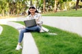 Technology and studentship concept. Cheerful lady student using laptop computer and wearing headphones, sitting outdoors Royalty Free Stock Photo