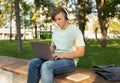 Technology and studentship concept. Male student using laptop computer and wearing headphones, sitting outdoors Royalty Free Stock Photo