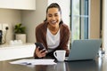 Technology, woman smile with smartphone and documents with laptop on kitchen counter of her home. Connectivity Royalty Free Stock Photo