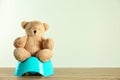 Teddy bear with blue potty on table against light background, space for text. Toilet training