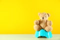 Teddy bear with blue potty on table against yellow background. Toilet training