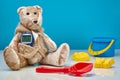 Teddy bear with a glucometer and scattered children`s toys on a blue background.