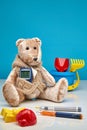 Teddy bear with a glucometer and scattered children`s toys and insulin pens on a blue and white background