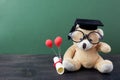 Teddy bear with graduation hat and diploma in front of green chalkboard. School concept Royalty Free Stock Photo