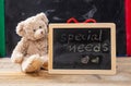 Teddy bear hiding behind a blackboard. Special needs text drawing on the blackboard