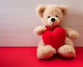 Teddy bear holding a red heart sitting on red floor. Valentines day Royalty Free Stock Photo