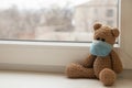 Teddy bear in a medical mask on the window in the apartment, children`s morbidity during
